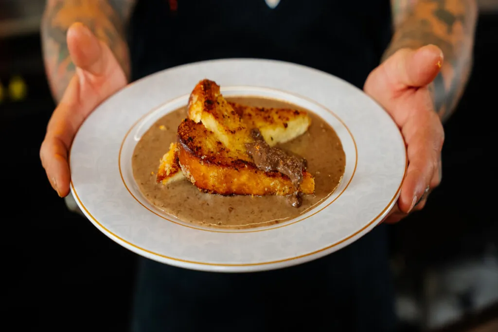 mãos segurando prato branco com duas fatias de rabanada com creme marrom de pasta de amendoim