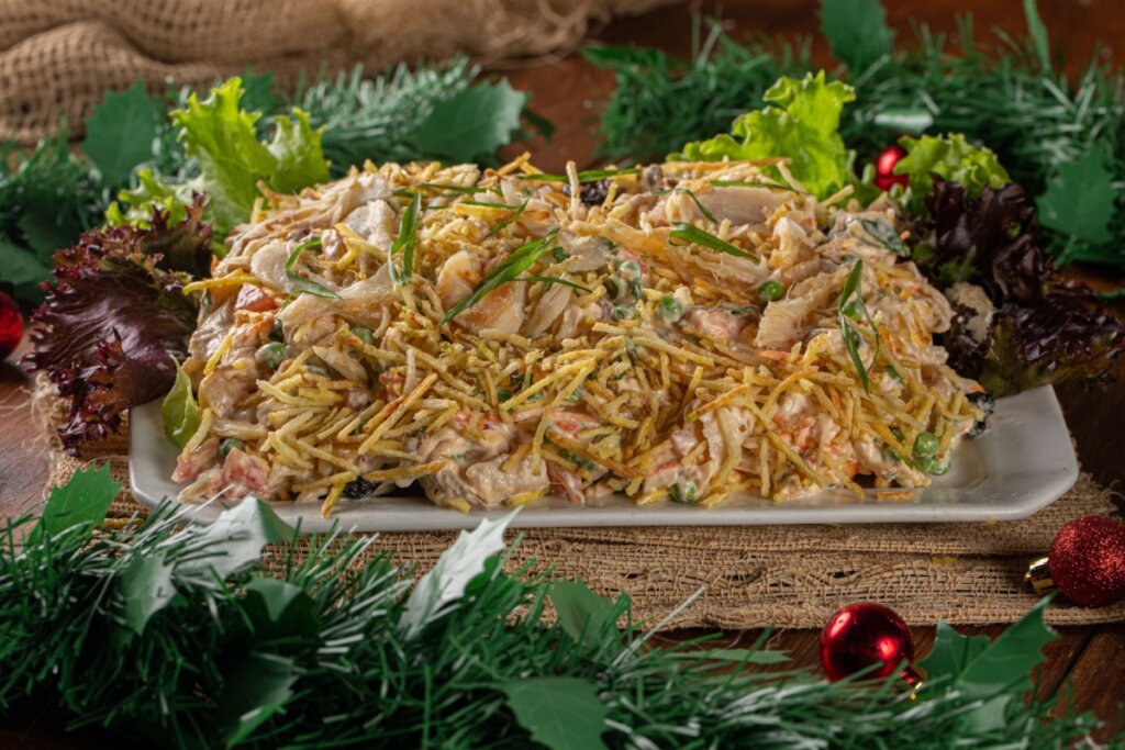 Salpicão servido em travessa de cerâmica branca com decoração de Natal ao redor em cima de mesa fe madeira