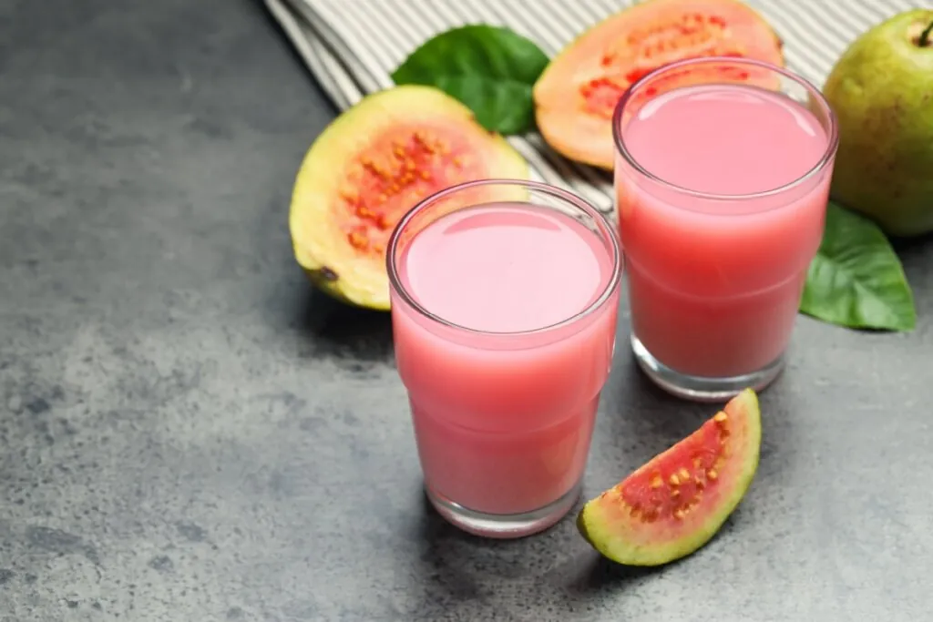 Dois copos de vidro com suco detox de goiaba ao lado de pedaços de goiaba e pano listrado