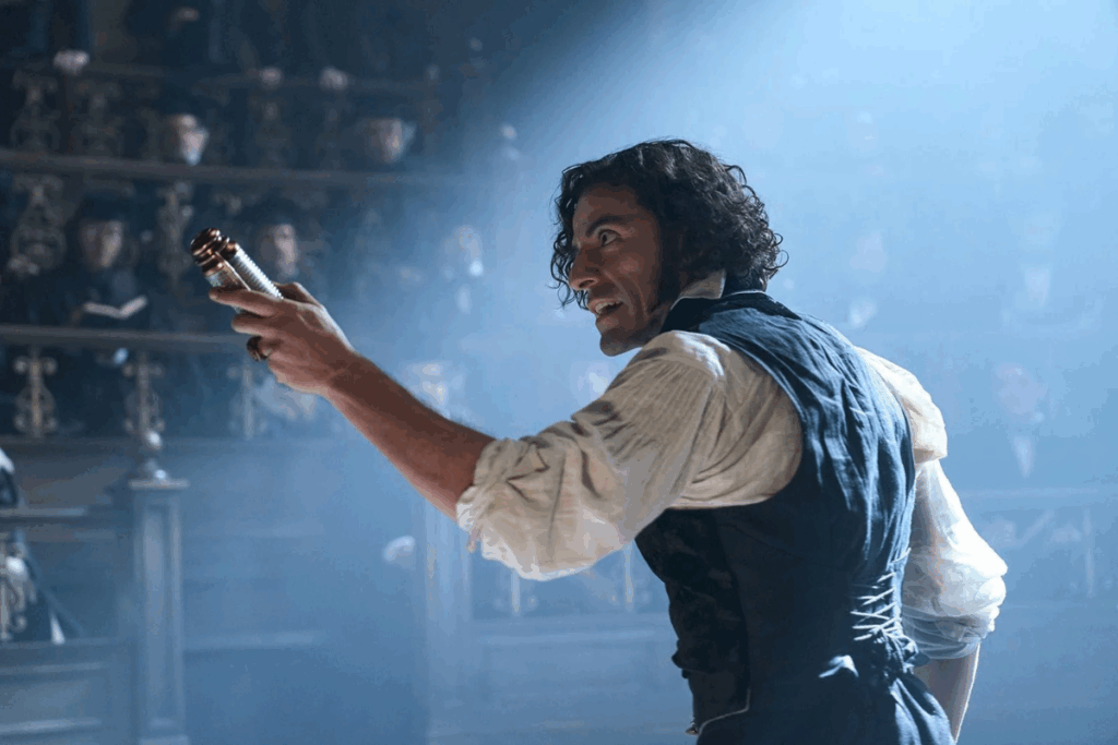 um homem de perfil com cabelos escuros e cacheados, vestindo trajes de época (colete escuro sobre camisa branca de mangas bufantes), segura um objeto cilíndrico metálico com determinação