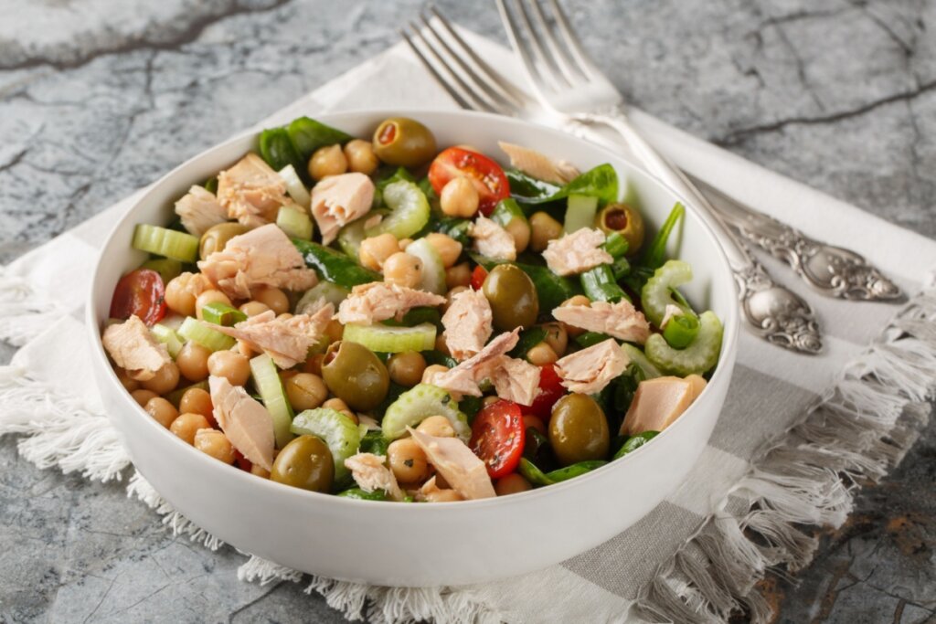 Tigela com salada de grão-de-bico misturada a atum em pedaços, pepino fatiado, tomates-cereja e azeitonas verdes