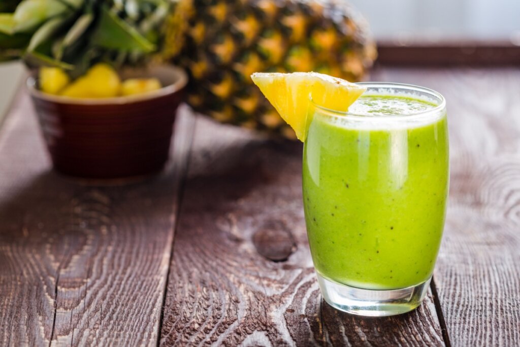 Suco de abacaxi com espinafre em um copo translúcido sobre uma mesa de madeira