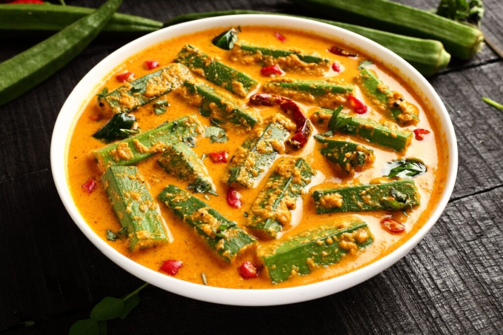 Curry de quiabo servido em tigela branca em cima de mesa de madeira