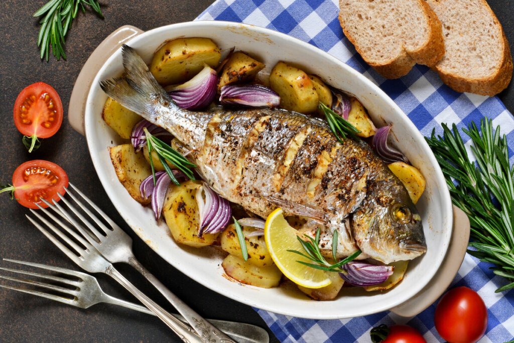 Travessa branca com peixe assado com batatas e cebola roxa