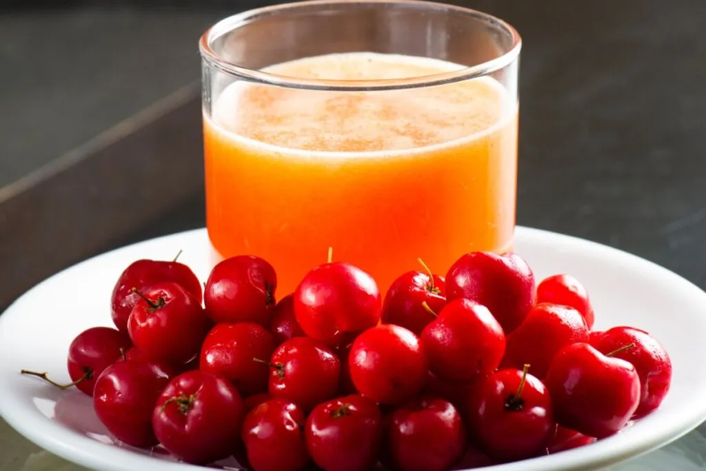 Prato branco com acerolas frescas e suco de acerola 