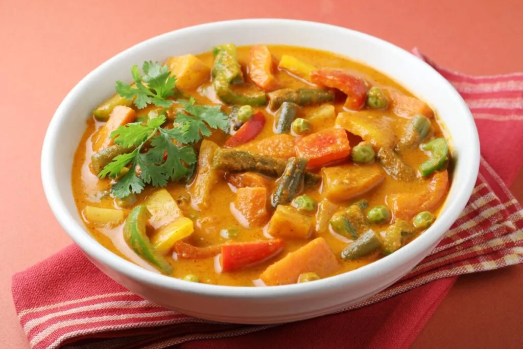 Curry de legumes cremoso servido em tigela branca em cima de mesa de madeira