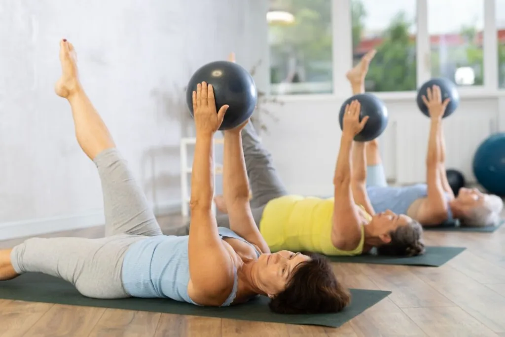 Mulheres usando roupa de academia, fazendo exercícios com bola em estúdio de pilates