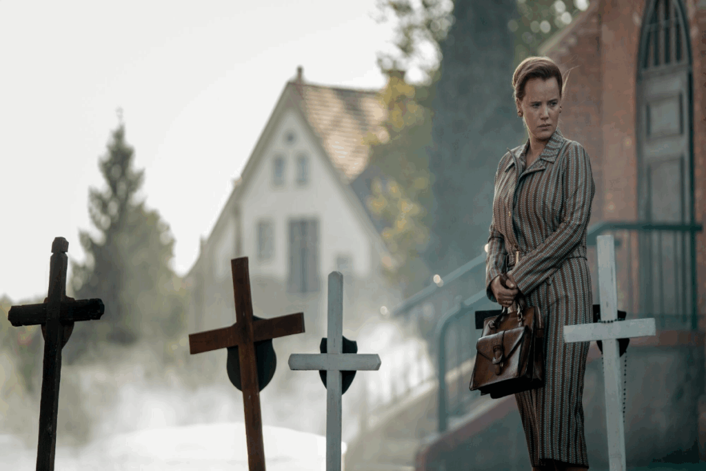 Uma mulher com roupa social listrada e cabelo preso em coque olhando para cruzes em túmulos de crianças