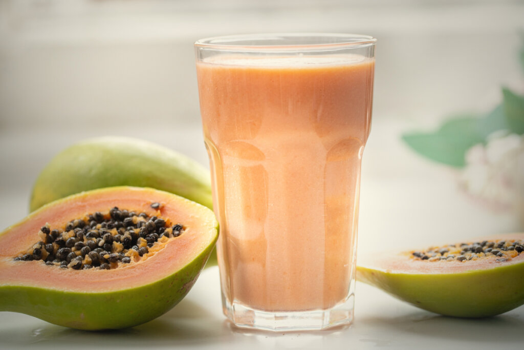 Copo de vidro com vitamina de mamão ao lado de mamão cortado na metade