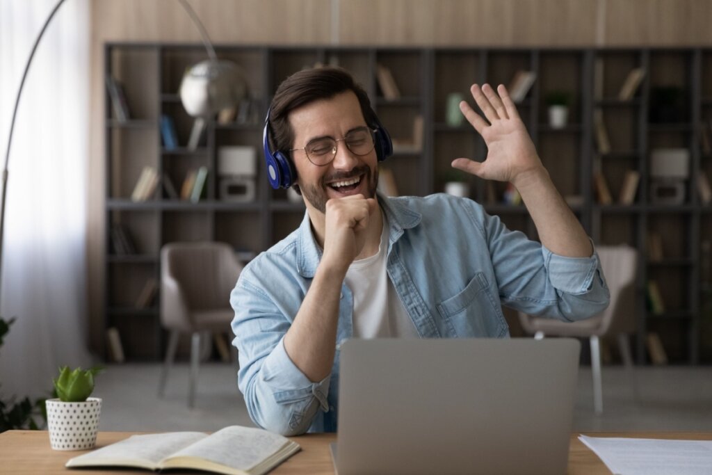 Homem com fones de ouvido cantando animado enquanto usa notebook em ambiente doméstico