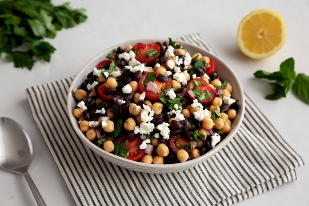 pote com salada de grão-de-bico, feijão-preto, tomate e queijo em cima de pano listrado