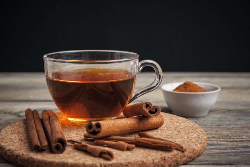 xícara de vidro com chá de canela, e pedaços de canela