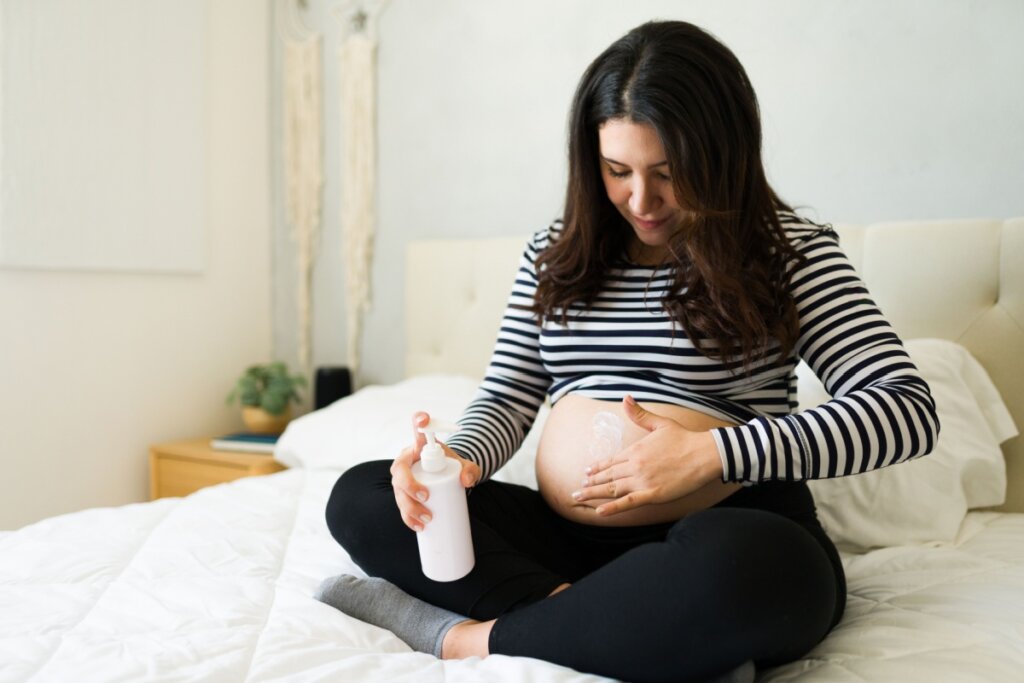 Grávida sentada passando creme na barriga 