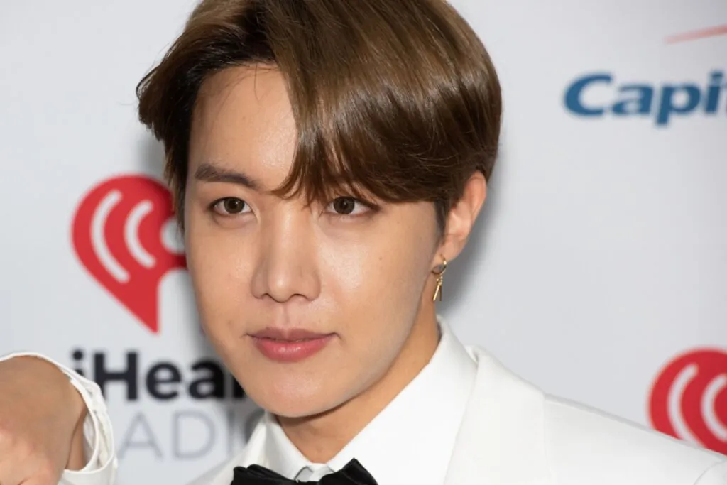 Homem com cabelo curto com franja castanho escuro, usando terno branco, camisa branca e gravata borboleta preta