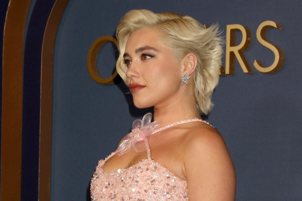 Florence Pugh, com corte bixie com ondas marcadas, usando vestido rosa com brilho e posado para foto