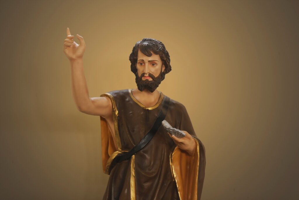 Estátua de São João com a mão levantada para cima, cabelos longos e barba 