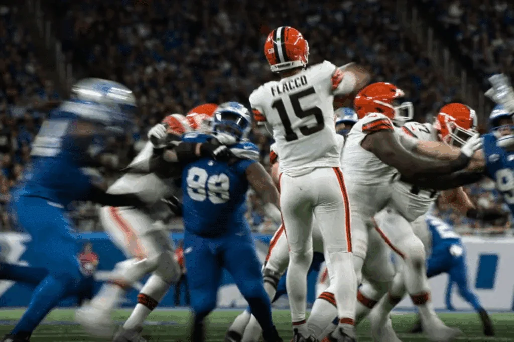 Em meio a um jogo movimentado da NFL, o quarterback com a camisa branca número 15 prepara um passe de costas para a câmera, cercado por jogadores em ação.