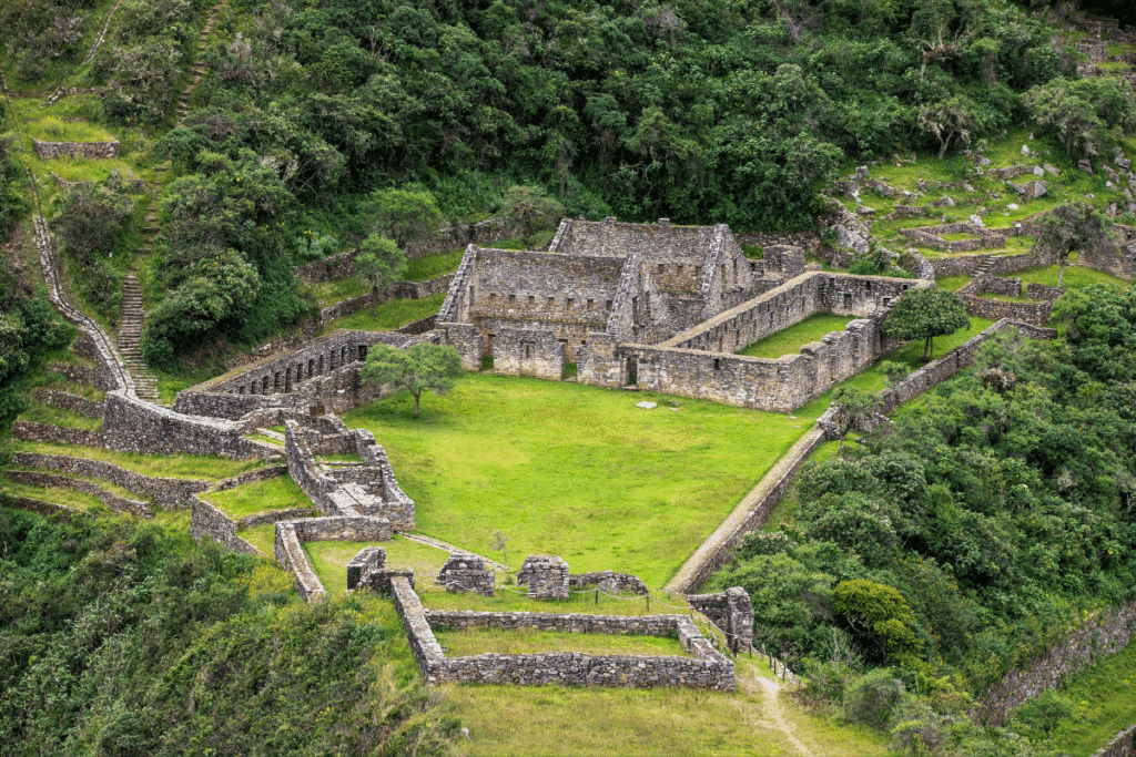 Vista do alto de ruínas incas de pedra construídas em patamares na encosta, cercadas por vegetação verde densa e gramados internos.