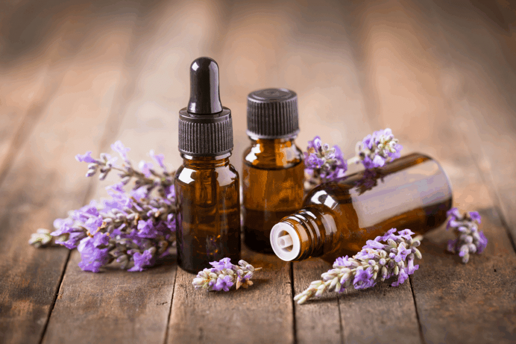 Três frascos de vidro âmbar estão sobre uma mesa de madeira, sendo um deles com conta-gotas. Ramos de flores de lavanda roxa estão dispostos ao redor dos frascos.